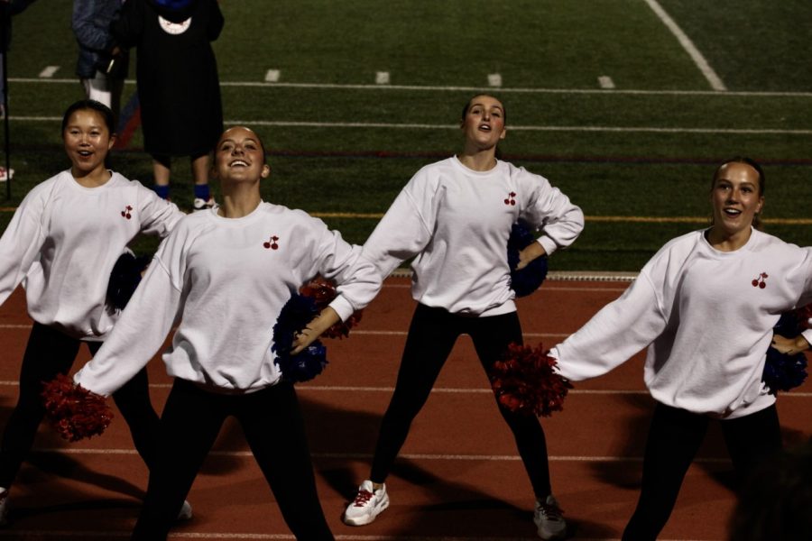 Anne Wang, Anna Barrett, Sofia Silva, and Halle Metcalf cheering on the crowd at a football game.