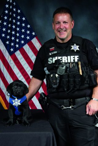 ON DUTY: Deputy Sheriff Officer and SRO Adam Nardi poses with Riley after Riley is sworn in by the Arapahoe County Sheriff as the district’s first therapy dog. “We go through [schools] and Riley is very popular,” Nardi said. “We talk to administrators and school mental health staff, and if there is a need [for a therapy dog,] we tell them to reach out to us.”