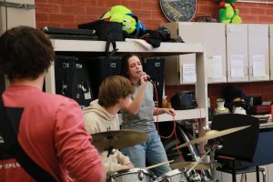 Senior Maggie Lee (right) sings “Waste of Time“ by Early Eyes during Purely Indigo’s practice for the Talent Show on Feb. 14 in the Creek band room while junior Drewes Emerson (left) plays bass and senior Nathan Krause plays the drums.