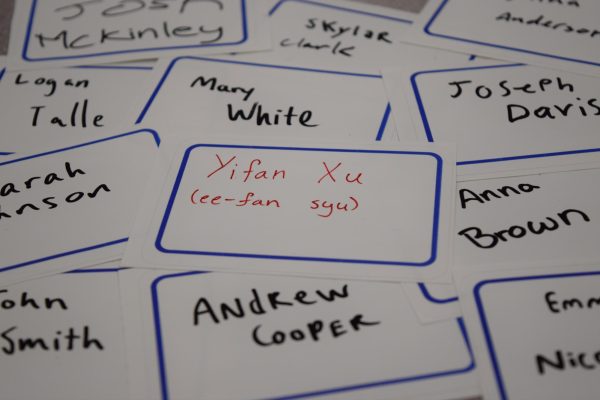 An assortment of name tags are scattered on a table, highlighting Yifan Xu, Chief Artist Angela Xus given name. Students with unique names feel that peers dont put enough effort into pronouncing them correctly.