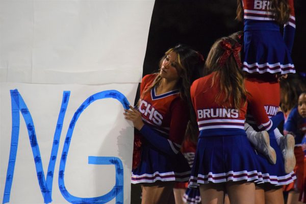 Members of Creeks cheer hold up the opening banner during the homecoming football game on Oct. 6. During games, many members of the cheer and poms team face discriminatory comments that dont match the amount of respect they deserve.