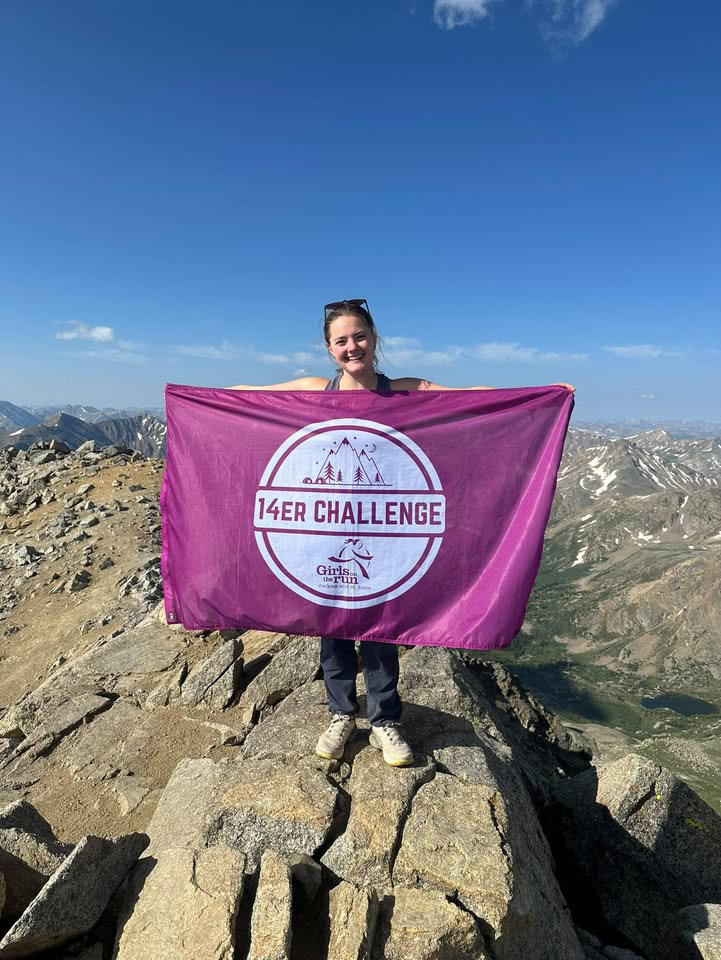 Creek alum Hannah Grober ('24) stands on the summit of Mt. Massive holding a Girls On The Run Flag.