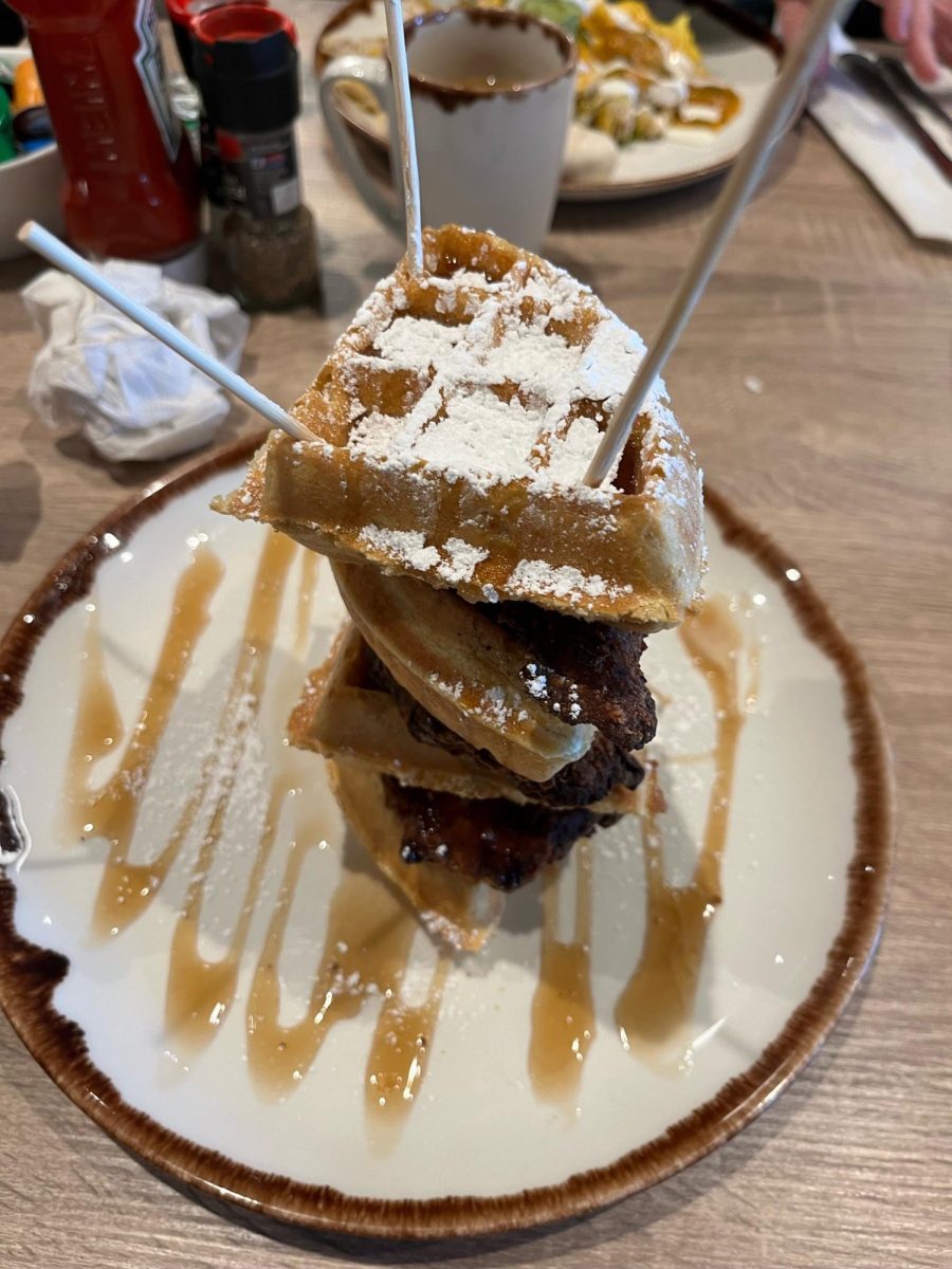 A beautiful stack of chicken and waffles, teeming with syrup and powdered sugar.