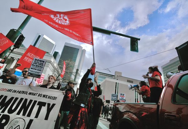 As speakers rally the crowd on the corner of 19th Street and Stout Street, a marcher hoists a flag, reading “AN INJURY TO ONE IS AN INJURY TO ALL,” a saying popularized by the Industrial Workers of the World to signify worker solidarity. The protest on May Day focused on labor unions, but also criticized the Trump administration for many grievances.