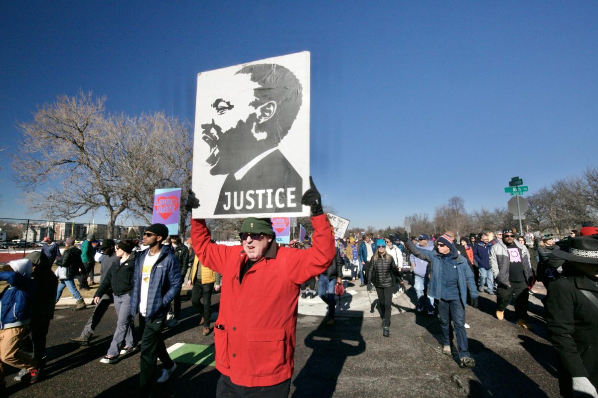 A man marches down Columbine St. in front of East High School, holding a sign picturing a spirited Martin Luther King, Jr.