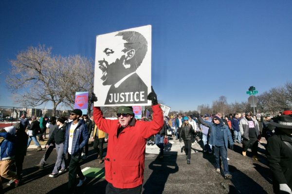 A man marches down Columbine St. in front of East High School, holding a sign picturing a spirited Martin Luther King, Jr.